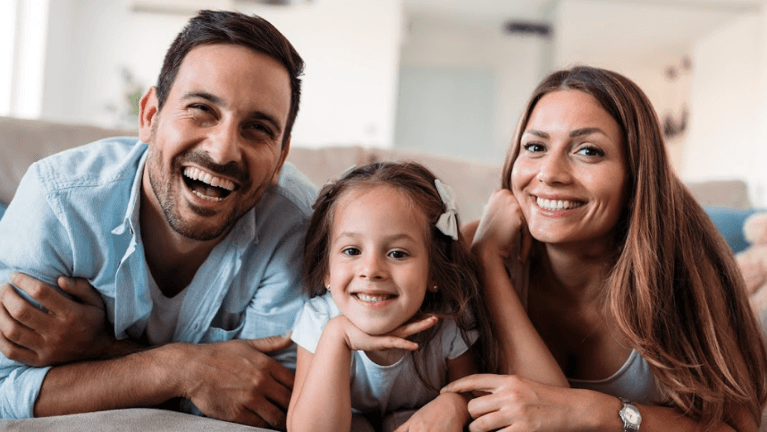 man and woman smiling with their daughter 