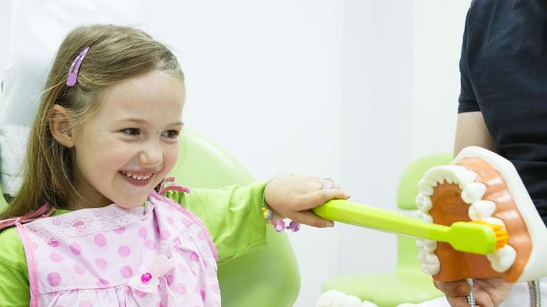 young girl brushing toy teeth with a large toothbrush