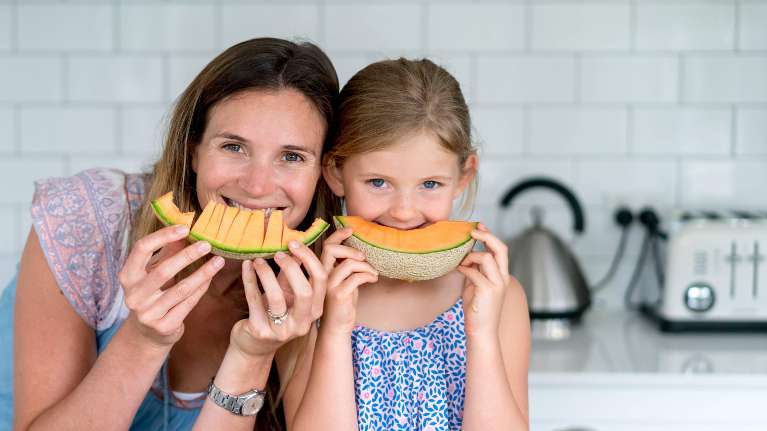 Mother and young daughter eating slices of cantaloupe 