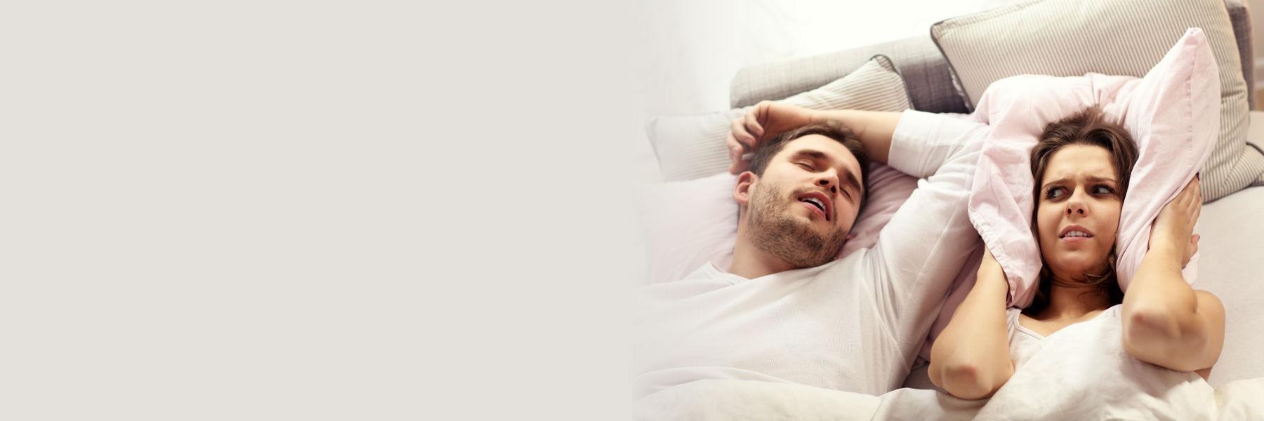 Man snoring next to wife while she holds a pillow over her ears in lincoln